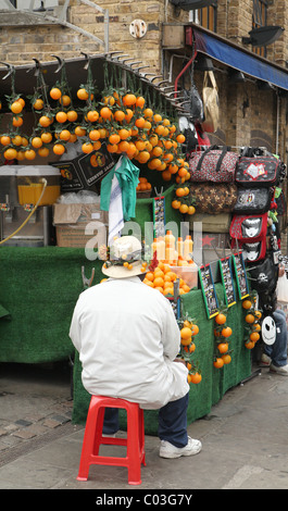 Orange Verkäufer in Camden Market auf roten Stuhl sitzend Stockfoto