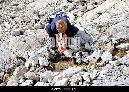 Zehn Jahre alter Junge aus einer Quelle von Wasser zu trinken, während einer Wanderung Berg Nebelhorn, Allgäuer Alpen, Bayern, Deutschland, Europa Stockfoto