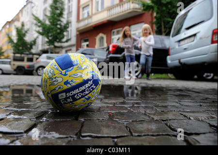 Zwei Mädchen laufen nach einem Ball auf einer Straße während des Spielens Stockfoto
