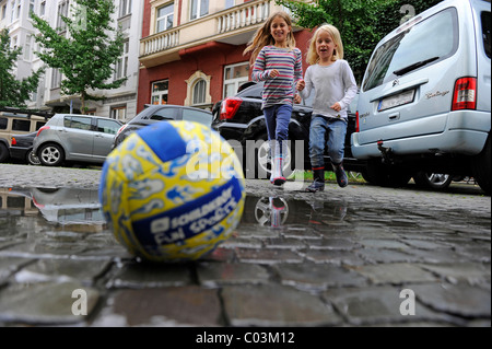 Zwei Mädchen laufen nach einem Ball auf einer Straße während des Spielens Stockfoto