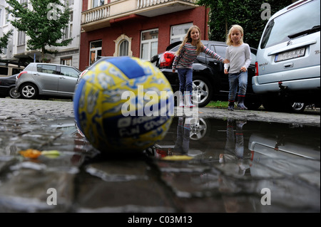 Zwei Mädchen laufen nach einem Ball auf einer Straße während des Spielens Stockfoto