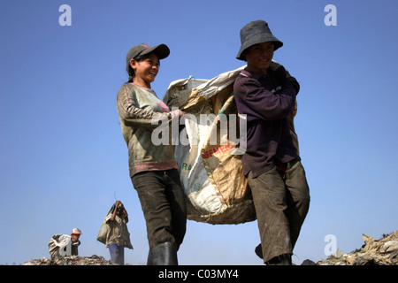 Ein junger Mann und eine Frau tragen eine große Tasche voller Müll auf einer verschmutzten Mülldeponie in Phnom Penh, Kambodscha. Stockfoto