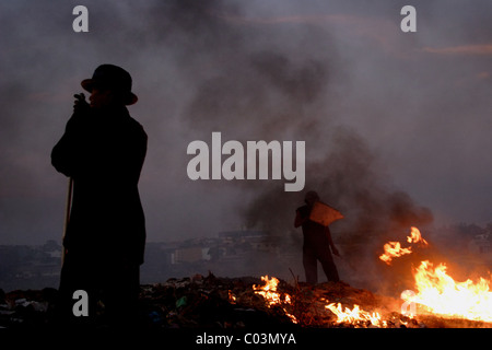 Ein Arbeiter schirmt sein Gesicht aus der Verbrennung von Müll wie ein anderer Mann in Phnom Penh auf Stung Meanchey Deponie in Kambodscha blickt. Stockfoto