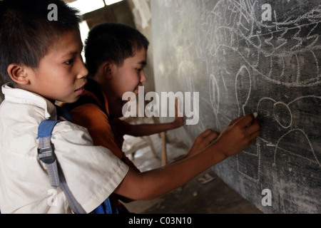 Eine Gruppe von jungen Studenten sind Zeichnung Bilder auf einer Tafel an einer heruntergekommenen Grundschule in kommunistische Laos. Stockfoto