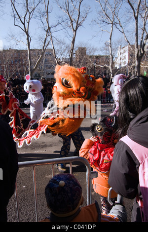 Young Boy in Lion Tanz Kostüm rutscht durch die Barrikade durchzuführen mit einem Orange Löwen im chinesischen Neujahrsparade in NYC Stockfoto