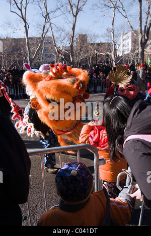 Young Boy in Lion Tanz Kostüm rutscht durch die Barrikade durchzuführen mit einem Orange Löwen im chinesischen Neujahrsparade in NYC Stockfoto