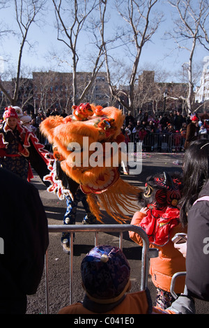 Young Boy in Lion Tanz Kostüm rutscht durch die Barrikade durchzuführen mit einem Orange Löwen im chinesischen Neujahrsparade in NYC Stockfoto