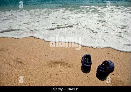 Ein paar Sandalen an einem Sandstrand der tropischen Strand mit weißem sanfte Wellen Rauschen Stockfoto