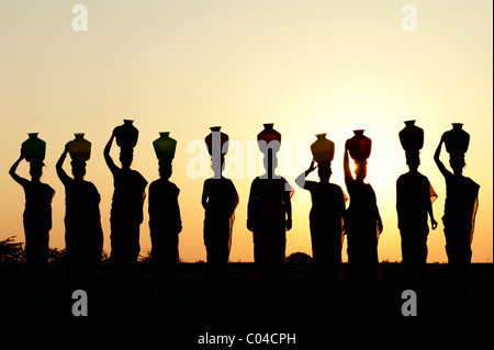 Gruppe von indischen Frauen stehen mit Wasser Töpfen auf ihren Köpfen in der indischen Landschaft. Silhouette Stockfoto