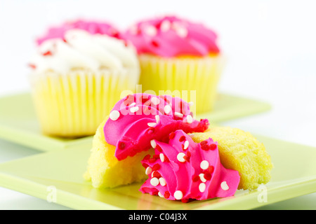 Im Vordergrund ist ein geschnittenen Cupcake mit rosa Zuckerguss auf eine leichte grüne Platte; der Hintergrund unscharf, bietet Farbe. Stockfoto