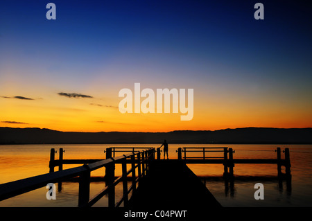 Eine Frau auf einem Steg im See Illawarra den Sonnenuntergang zu beobachten. Stockfoto