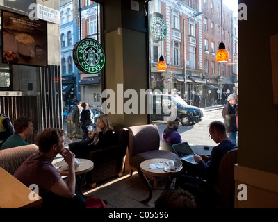 Starbucks Innenraum-Kunden, die in der Lounge sitzen, trinken Kaffee und Mann mit einem Laptop-Computer in Soho London England, Großbritannien KATHY DEWITT Stockfoto