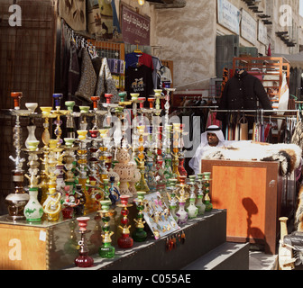 Qatari Ladenbesitzer wartet auf Kunden im Souq Waqif, Doha, Katar, neben bunten Wasserpfeifen und Kleidungsstück souvenirs Stockfoto