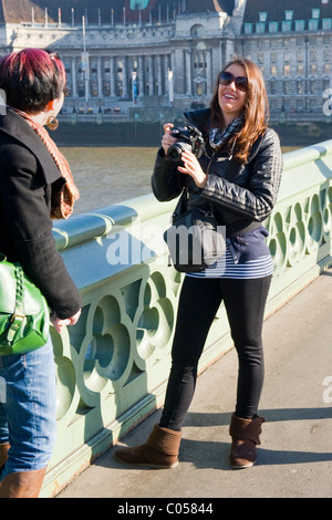 Hübsche junge Brünette Dame oder Mädchen in Leggins nimmt Foto des London Eye, Westminster Bridge mit Sony-Kamera in der Nähe von County Hall Stockfoto