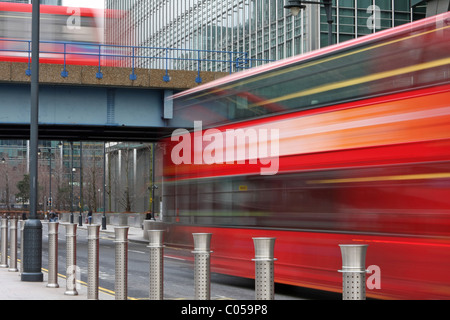 Ein verschwommenes Bus unter eine Brücke und einen unscharfen DLR-Zug gehen über die Brücke in Londons Canary Wharf Stockfoto