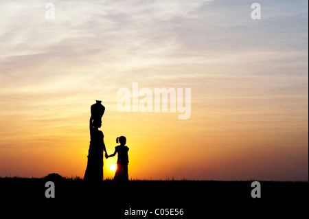 Indische Mutter mit Wassertopf mit Kind in der indischen Landschaft bei Sonnenuntergang. Silhouette Stockfoto