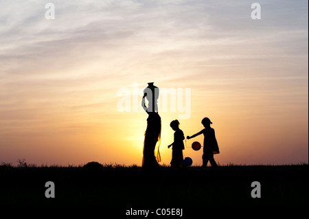 Indische Mutter mit Wassertopf mit Kinder und Luftballons in der indischen Landschaft. Silhouette Stockfoto