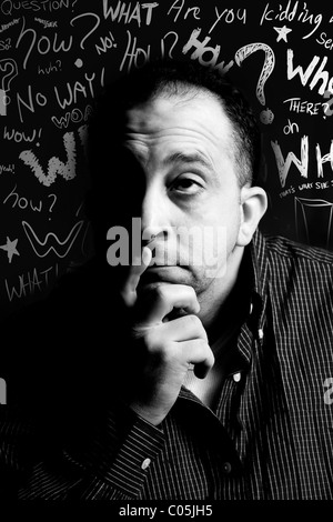 Ein gealterter Mann im Low-Key-Beleuchtung Nachdenken über etwas mit Fragewörtern im Hintergrund - schwarze und weiße Kritzeleien Mitte. Stockfoto