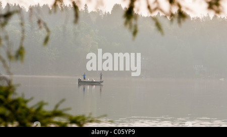 Angeln im See Sonnenaufgang. Zwei Männer stehen in ein kleines Boot Angeln an einem nebligen See kurz nach Sonnenaufgang. Stockfoto