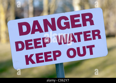 Eine krumme Warnschild auslesen "Gefahr tiefen Wasser halten" auf eine Regenwasser-Behälter in einem englischen Dorf. Stockfoto