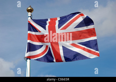 Ein Anschluß-Markierungsfahne oder "Union Jack" auf eine Fahnenstange in einem englischen Dorf vor einem blauen Himmel mit flauschigen Wolken fliegen. Stockfoto