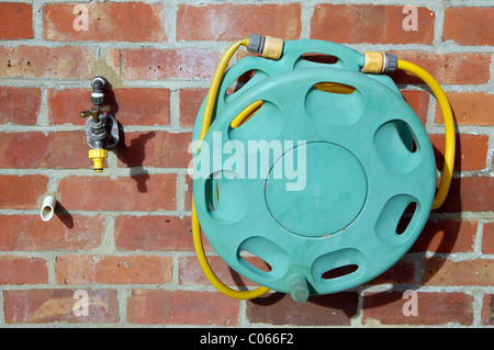 Ein Wasserhahn, mit Schlauchanschluss, und einem Schlauch Haspel auf der Mauer eines britischen Hauses. Außerdem gibt es eine Zisterne Überlaufen-Leitung. Stockfoto