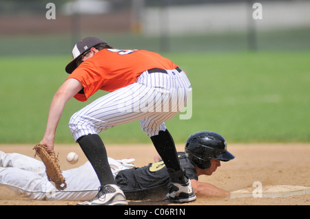 Erste Basisspieler kann Sie aus zu sichern werfen wie die Base Runner taucht zurück sicher in der Tasche während einer High School Baseball Spiel USA. Stockfoto