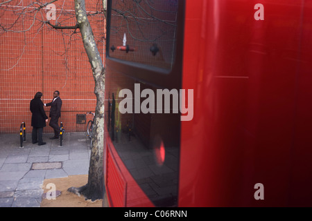 Zwei männliche Raucher stehen im Chat außerhalb ihrer Universitätsgebäude, gesehen vom Oberdeck eines London-Bus. Stockfoto