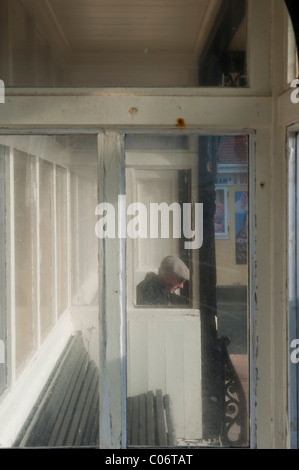 Ein Alter Mann sitzt in einem Windschutz an Hastings Küste East Sussex UK Stockfoto