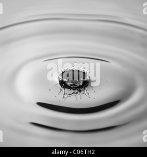 Ein monochromes Bild eines Tropfens Wasser mit einem Platzen der Blitz eingefroren, da er auf der Wasseroberfläche landet Stockfoto