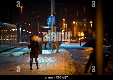 Eine Frau raucht eine Zigarette vorläufig stoppen Spaziergänge über verdichtetem Schnee und Eis auf eine Straßenbahn im Stadtzentrum von Dublin, am frühen Morgen. Stockfoto