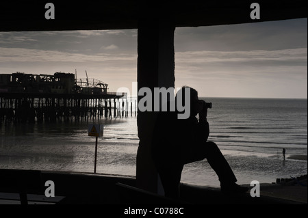 Ein Mann nimmt ein Foto an Flasche Gasse Hastings mit dem verbrannten Pier im Hintergrund Stockfoto