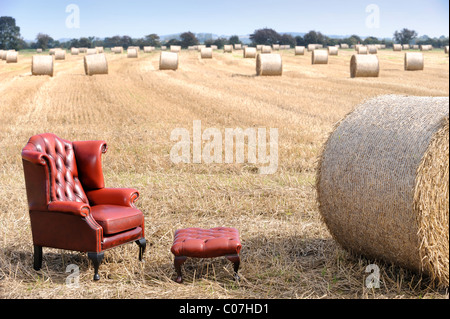 Eine antike rote Ledersessel in einem Feld von geerntetem Heu UK Stockfoto
