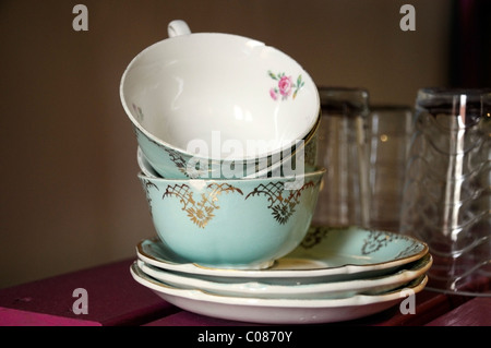 drei antike Tassen, Untertassen und Gläser auf einem rosa Regal bei Tageslicht. Stockfoto