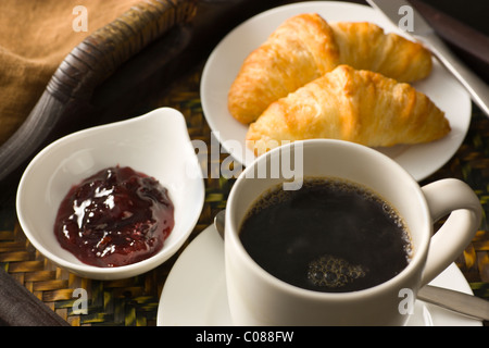 Ein Tablett mit Croissants, Marmelade und eine Tasse heißen schwarzen Kaffee Stockfoto