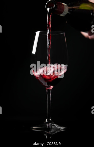 Ein Glas Rotwein aus der Flasche gegossen wird, auf einem schwarzen Hintergrund. Stockfoto