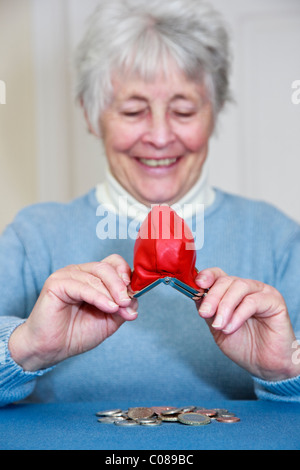 Wohlhabende senior ältere Frau mit einem zufrieden Ausdruck entleeren einen Haufen Geld aus der Handtasche vor. England, UK, Großbritannien Stockfoto