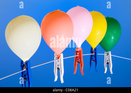 Gruppe von gefärbtem Wasser gefüllten Ballons hängen auf einer Wäscheleine mit blauem Himmel als Hintergrund, von unten gesehen Stockfoto