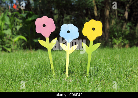 Drei bunte künstliche Blumen auf dem Rasen-Hintergrund Stockfoto