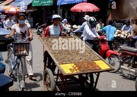 Eine Frau Lebensmittel Hersteller drängt einen Wagen beladen mit Schnecken auf einer belebten Straße in Phnom Penh, Kambodscha. Stockfoto