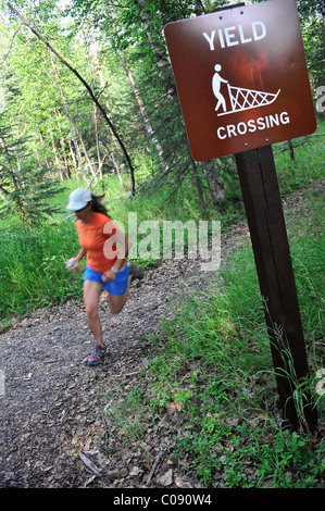 Weibliche Jogger führt vorbei an einem Hundeschlitten kreuzen Zeichen auf dem fernen Norden Bicentennial Park Trail in Anchorage, Alaska Yunan Stockfoto