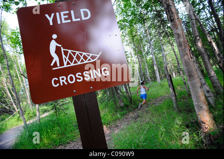 Weibliche Jogger führt vorbei an einem Hundeschlitten kreuzen Zeichen auf dem fernen Norden Bicentennial Park Trail in Anchorage, Alaska Yunan Stockfoto