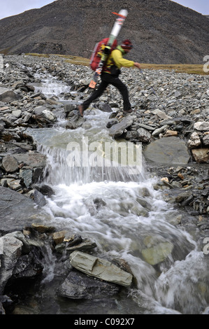 Backpacker überquert einen Bach im Rückkehr aus Mount Chamberlin Skiabfahrt, Brooks Range, ANWR Katak Creek-Tal Stockfoto