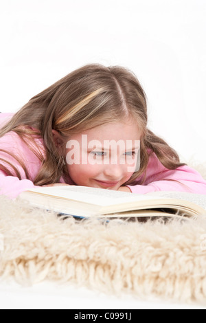 Mädchen, 8 Jahre, auf ein Shag Teppich liegen und ein Buch zu lesen Stockfoto