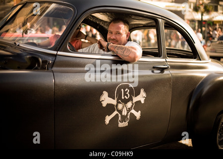 Ein junger Mann mit Tattoos Lächeln von innen einen Oldtimer bedeckt in Schädel und gekreuzten Knochen. Stockfoto