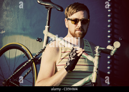 A fixed gear rider in a yellow striped tank top and sunglasses poses. Stockfoto