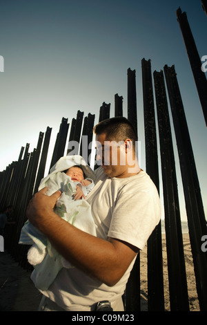 ein Mann hält sein Baby mit Zaun, der auf seinem Rücken an der Grenze in Tijuana, Mexiko Mexiko und USA trennt. Stockfoto