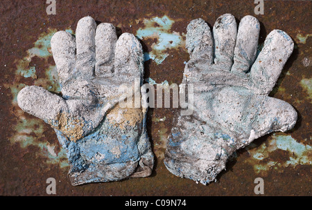 Paar stark verschlissene Arbeitshandschuhe auf rostigen Metallplatte Stockfoto