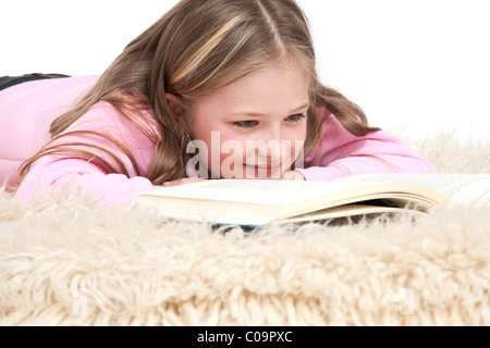 Mädchen, 8 Jahre, auf ein Shag Teppich liegen und ein Buch zu lesen Stockfoto