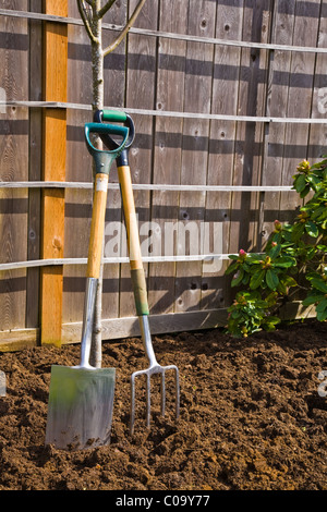 Ein Garten Gabel und Schaufel lehnte sich gegen einen Baum in einem frisch gelockerten Garten Stockfoto